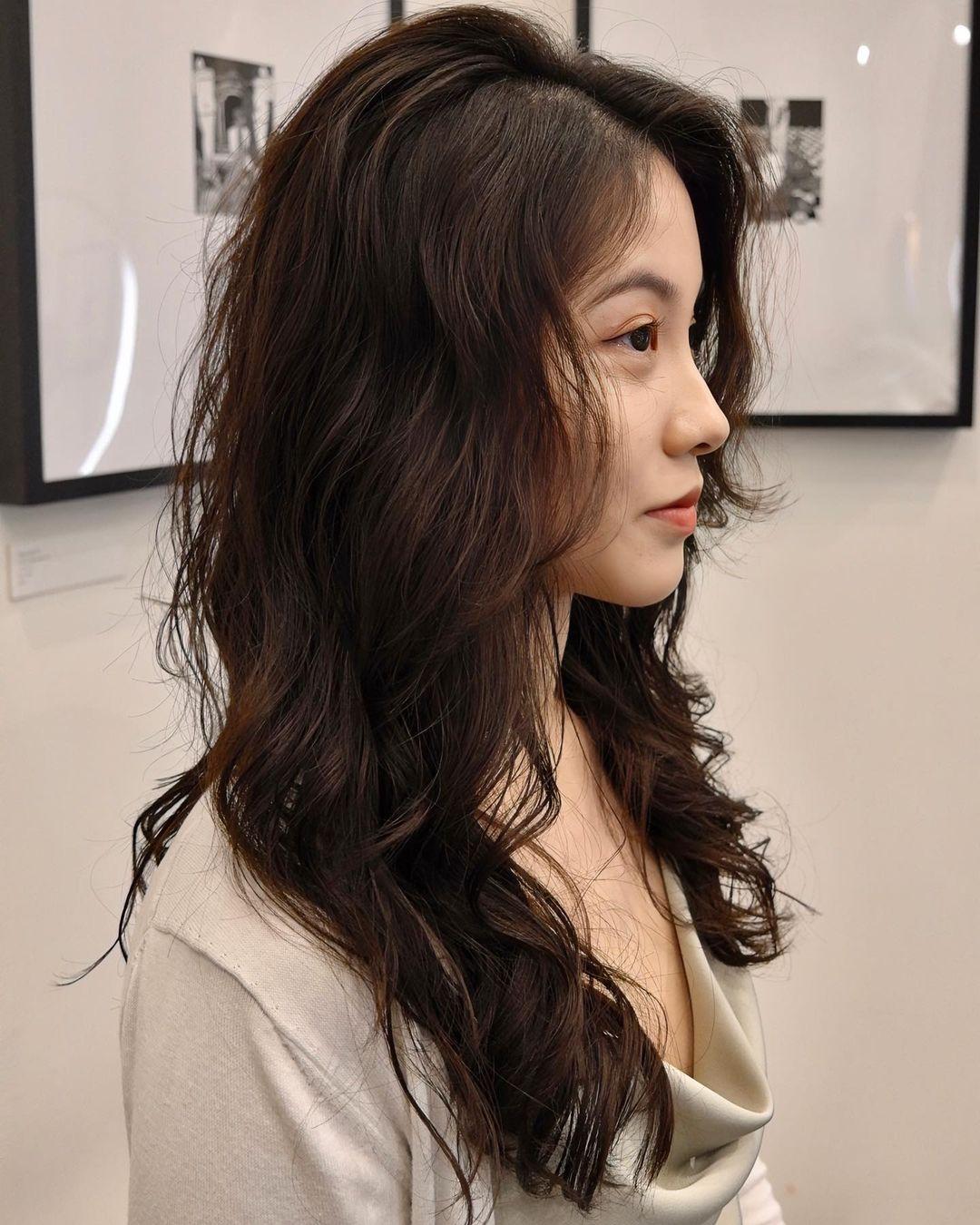 Long, dark brown hair cascades in soft, wavy layers with voluminous locks and side-swept bangs. 👩🏻‍🦱Hair by @hiro.nonstop 👩🏻‍🦱 3
