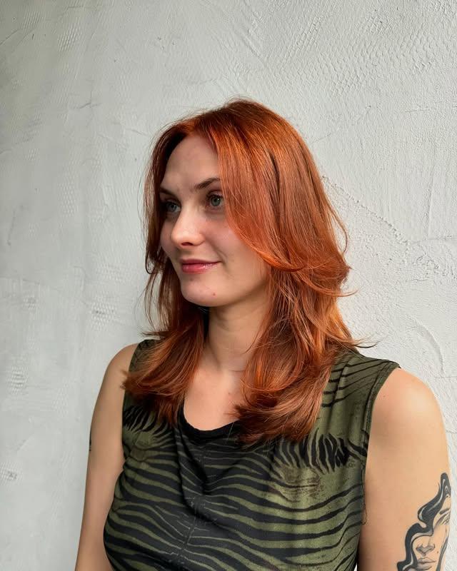 Layered copper butterfly haircut featuring soft, face-framing layers for a flattering silhouette.