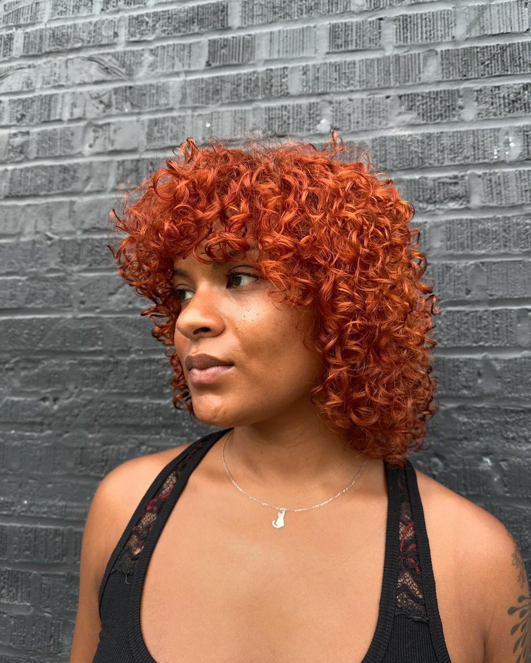 A medium-length curly bob with a vibrant copper-red color, offering voluminous and bouncy curls. 1