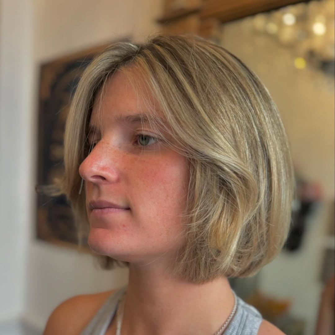 A short, straight bob with soft layers and a center part, featuring a warm blonde hue with honey highlights. 1