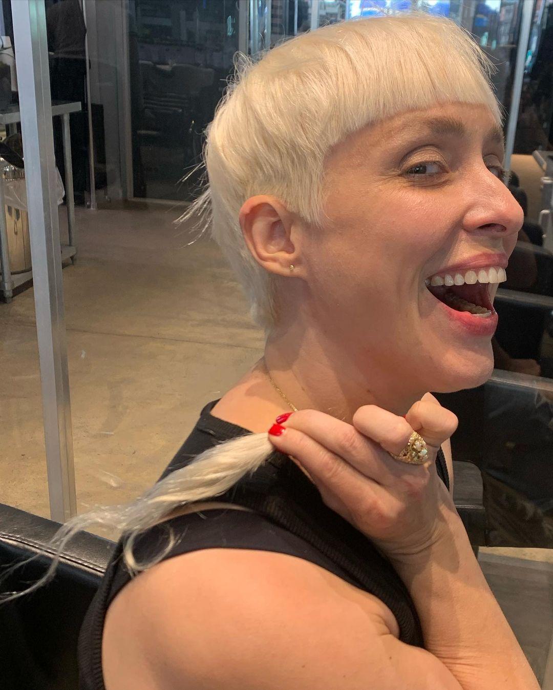 Short, straight platinum blonde hair styled in a pixie cut with distinguishing micro bangs. 2