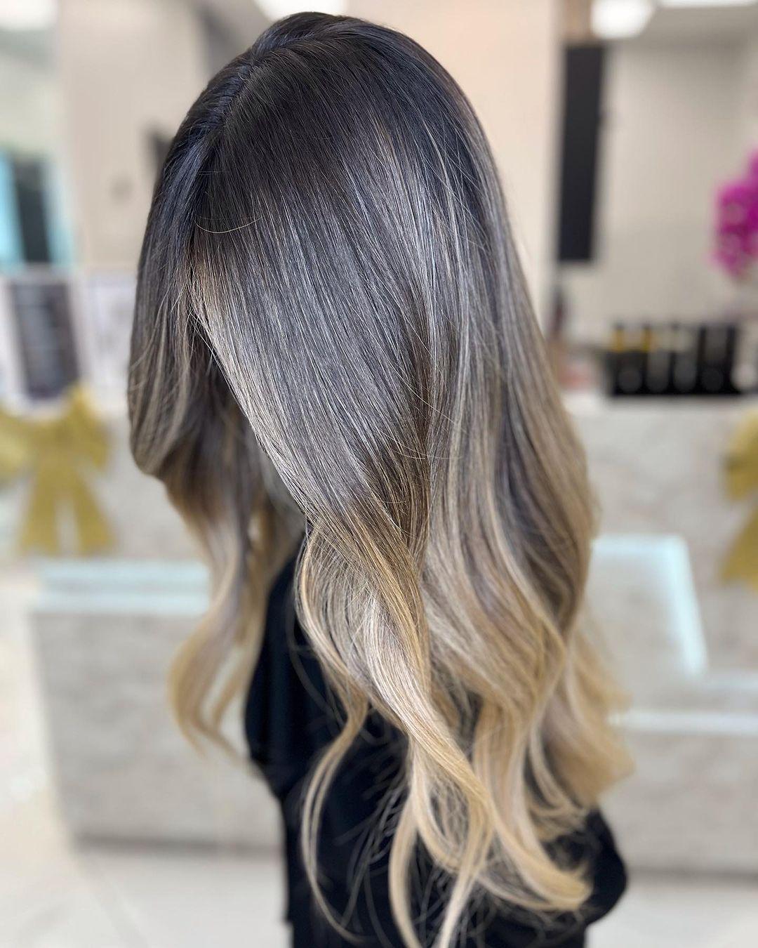 The hairstyle features long, wavy hair crafted with a dark blonde base and gradual platinum and ash blonde balayage highlights, styled in soft beach waves. 3