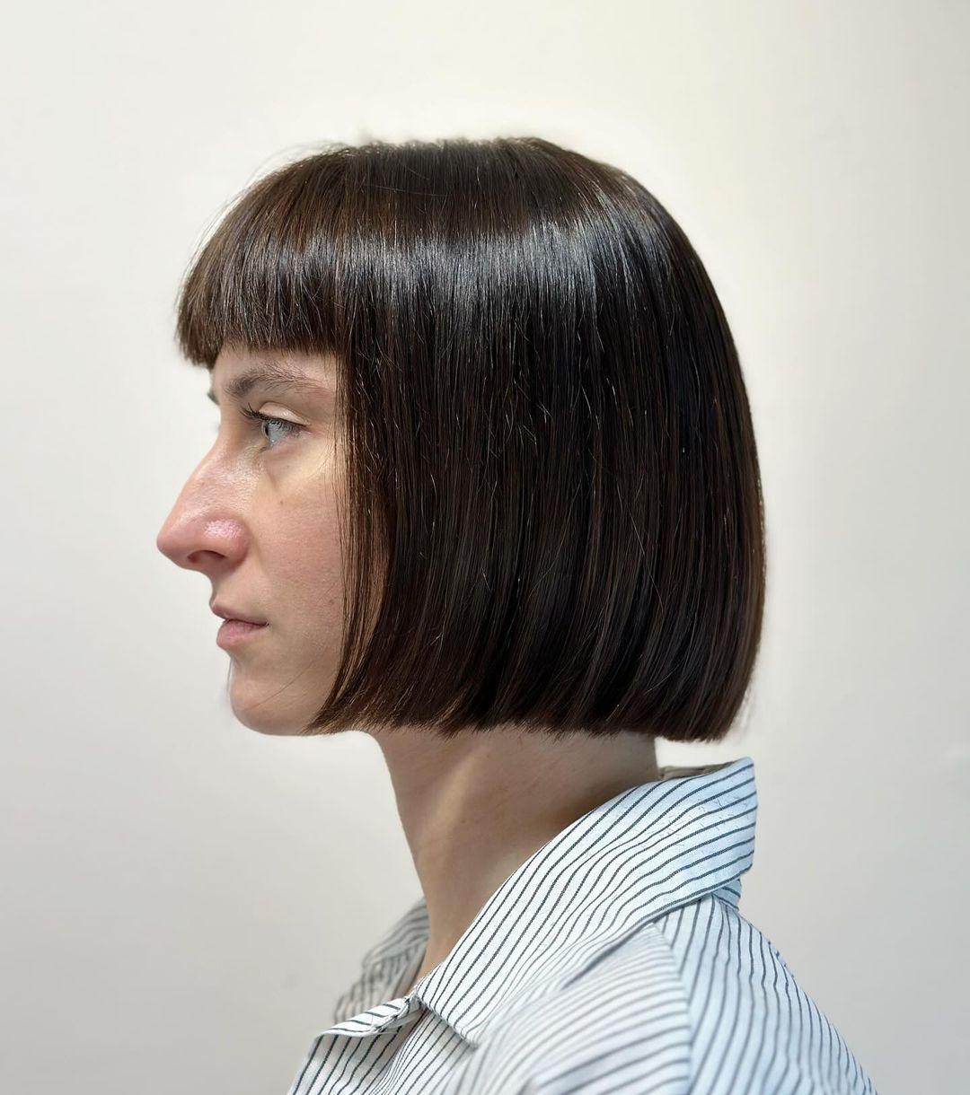 A sleek, short bob with blunt bangs and a symmetrical shape, characterized by sharp edges and a glossy brown finish. 2