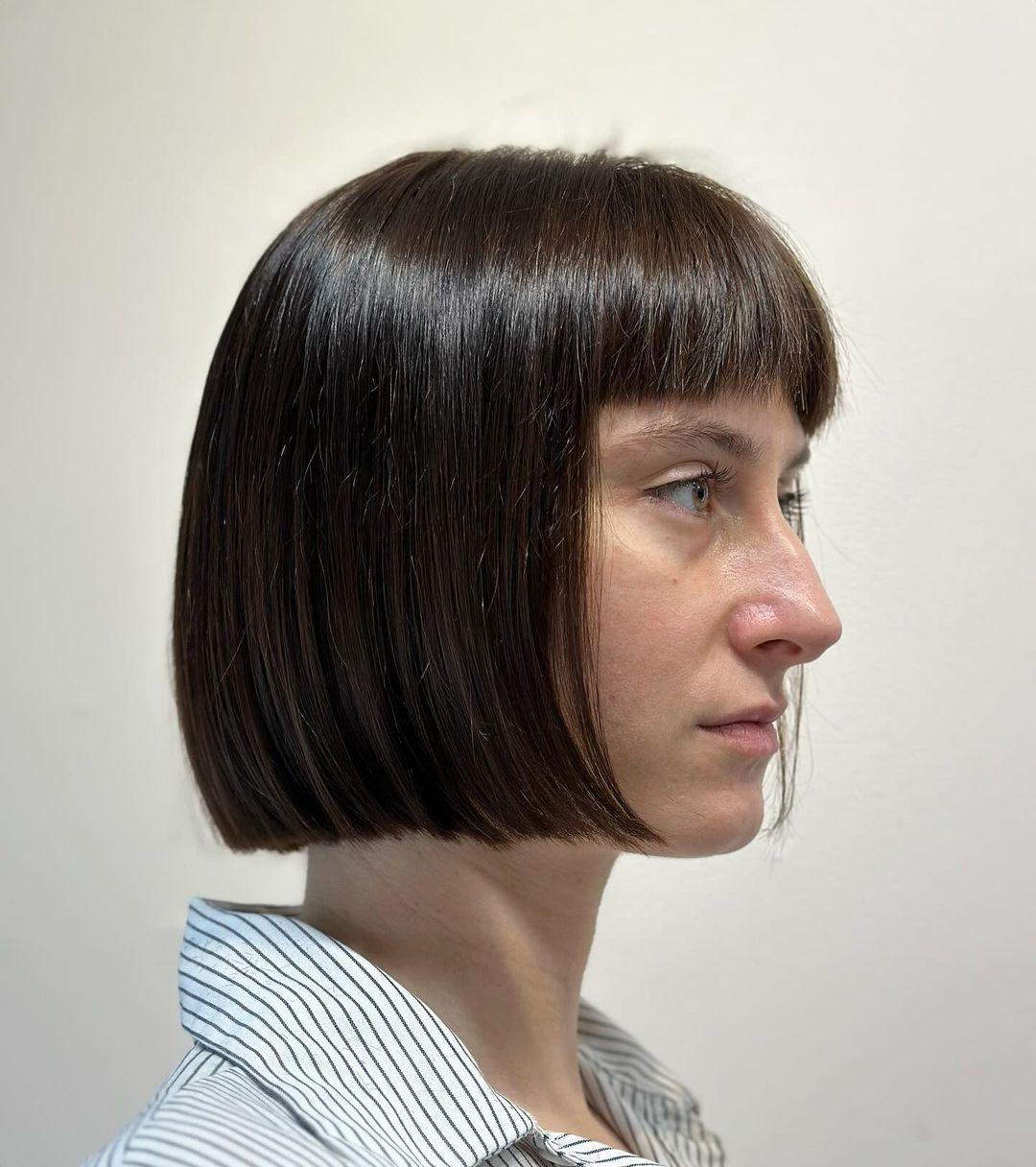 A sleek, short bob with blunt bangs and a symmetrical shape, characterized by sharp edges and a glossy brown finish. 3