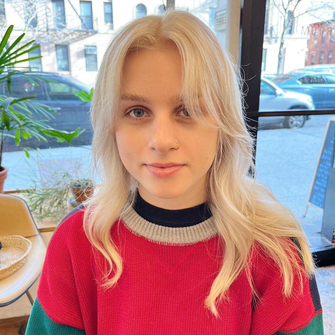 The hairstyle features long, platinum blonde hair with a wavy texture. It includes soft layers, face-framing layers, and curtain bangs. 🤍💛🤍#whiteblondehair by @limi.nyc  1