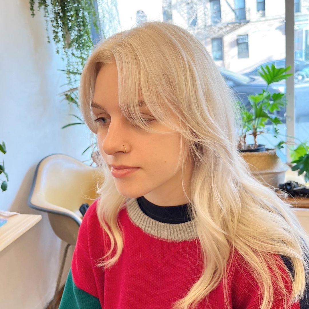 The hairstyle features long, platinum blonde hair with a wavy texture. It includes soft layers, face-framing layers, and curtain bangs. 🤍💛🤍#whiteblondehair by @limi.nyc  2