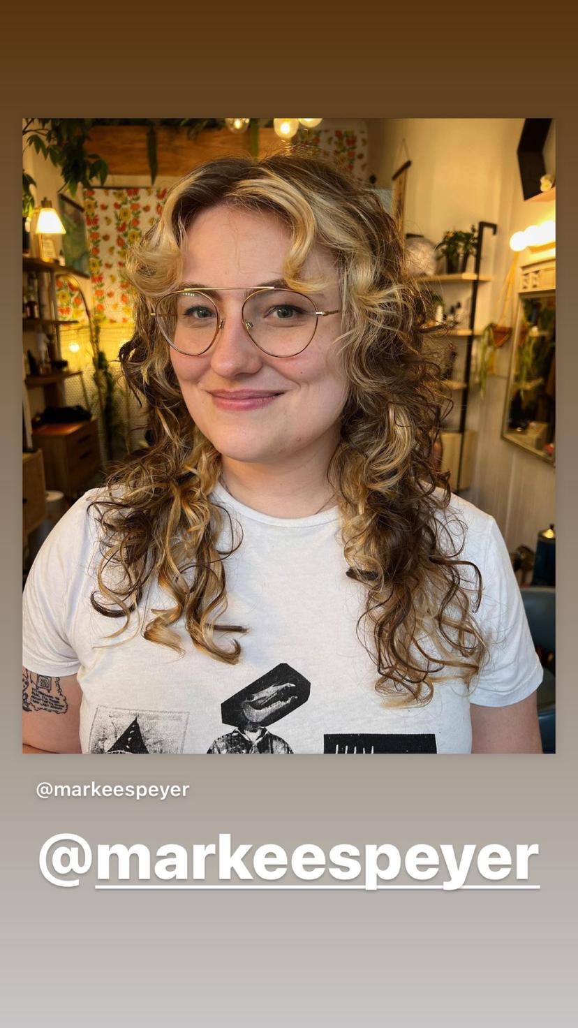 A textured wolf cut with lots of layers and curly curtain bangs in a bronde color.