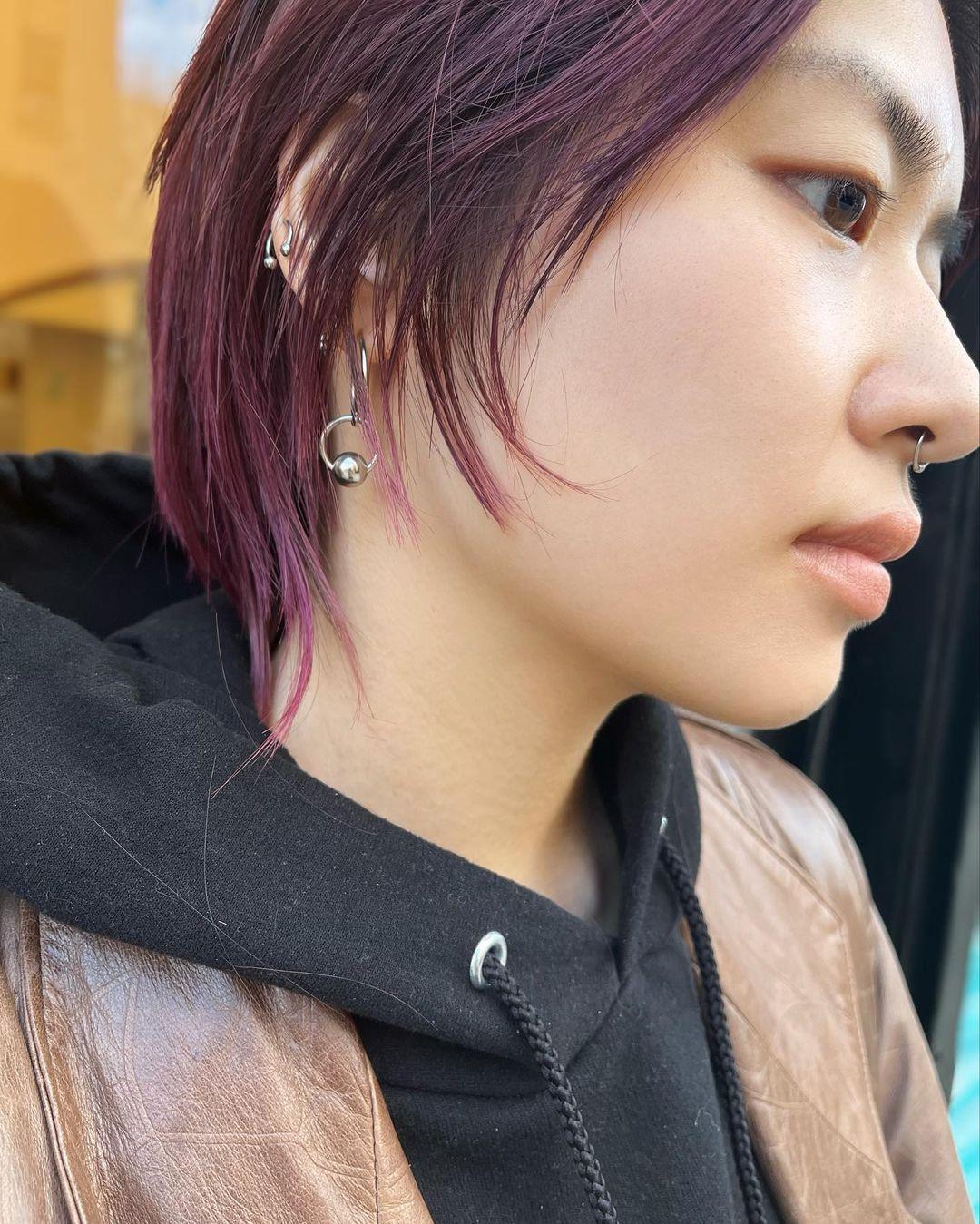 A chic and edgy short hairstyle with a layered cut that falls to ear-length, featuring side-swept bangs. The hair color is dark brown with vibrant plum highlights. 3