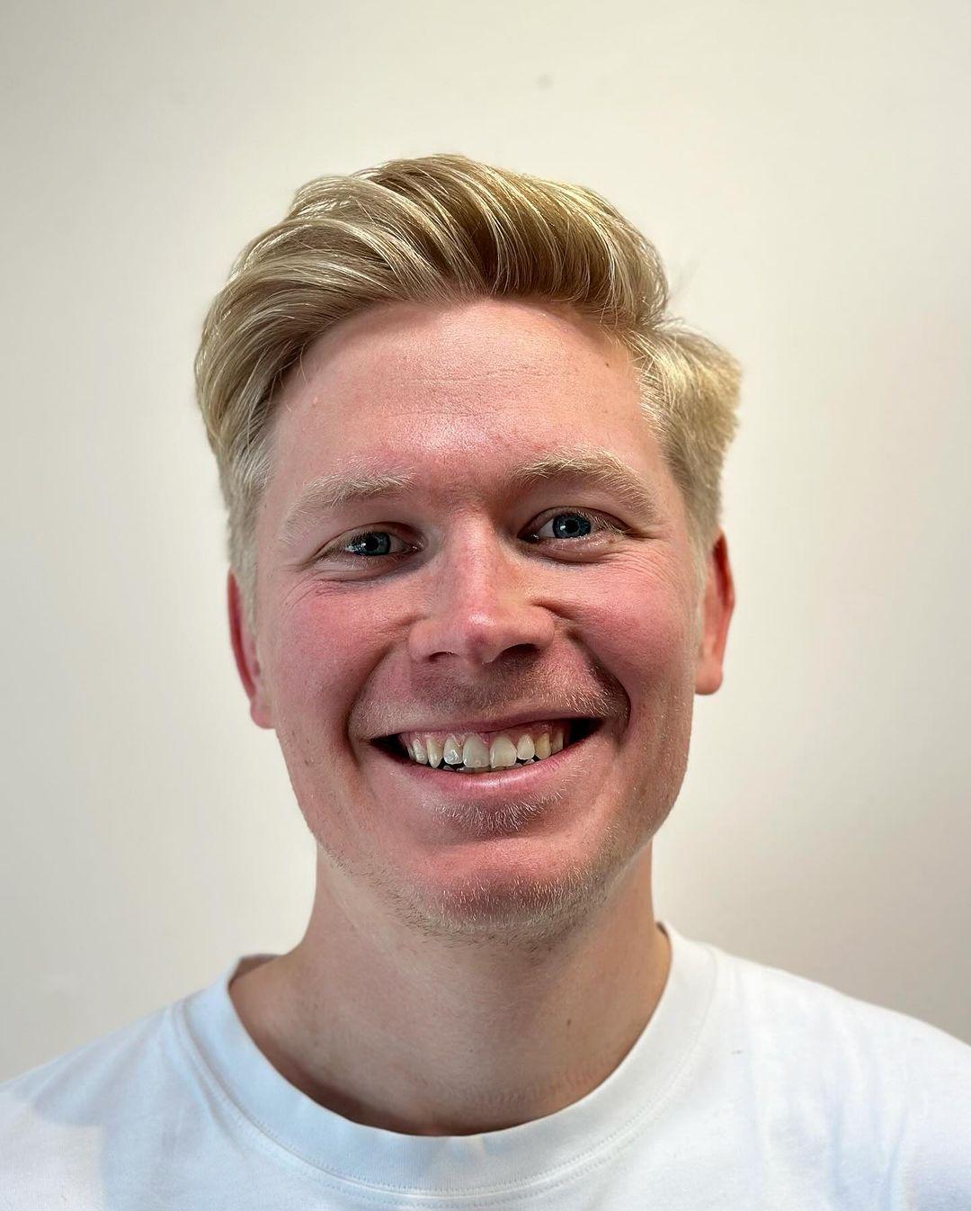 A sleek and short blonde hairstyle with tapered sides and a textured top, featuring a subtle side part. 2