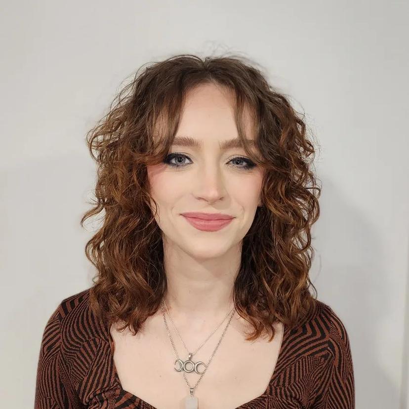 Medium-length chestnut to auburn curly hair with loosely defined curls and natural waves, providing textured volume.