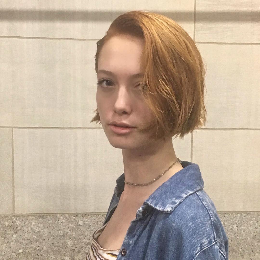 An edgy slope bob haircut with straight, short, red auburn hair. This asymmetrical bob features a side-part, giving it a modern and chic appearance. 1