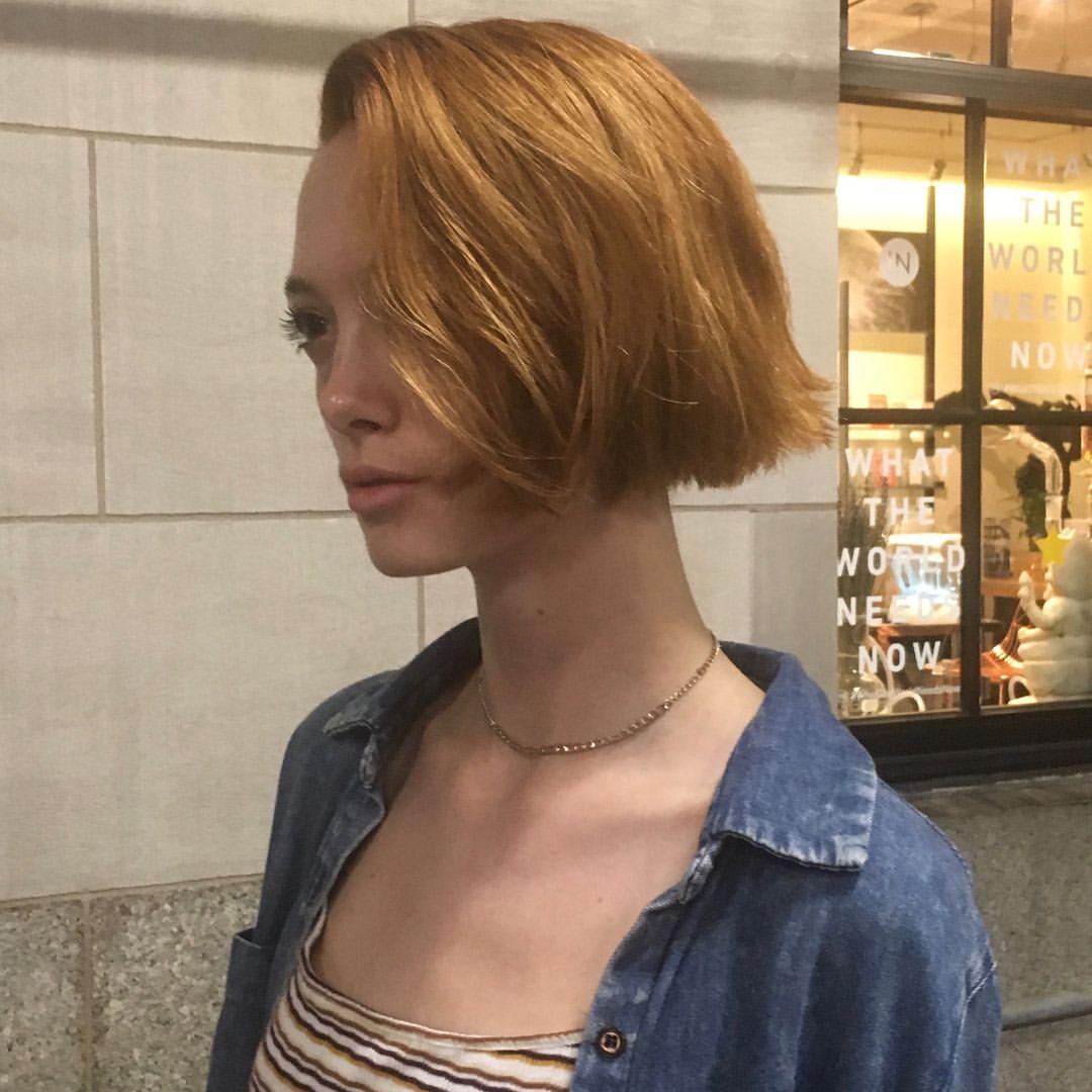 An edgy slope bob haircut with straight, short, red auburn hair. This asymmetrical bob features a side-part, giving it a modern and chic appearance. 2