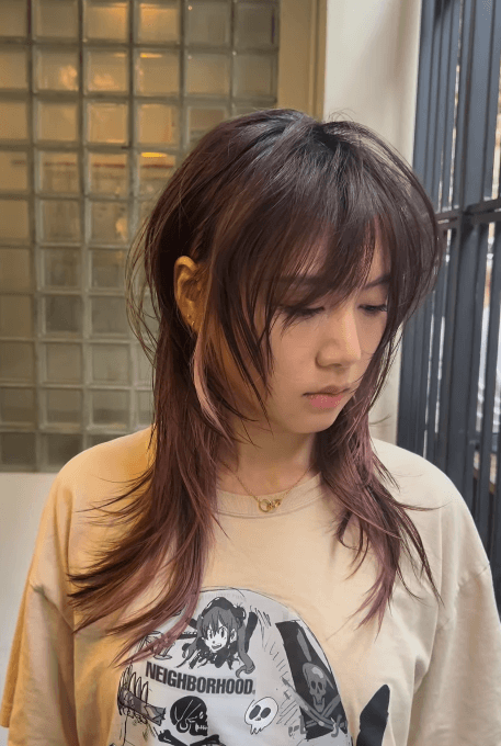Medium-length wavy hair with dark brown and light pink highlights, featuring soft cascading layers framing the face in a Butterfly Cut.