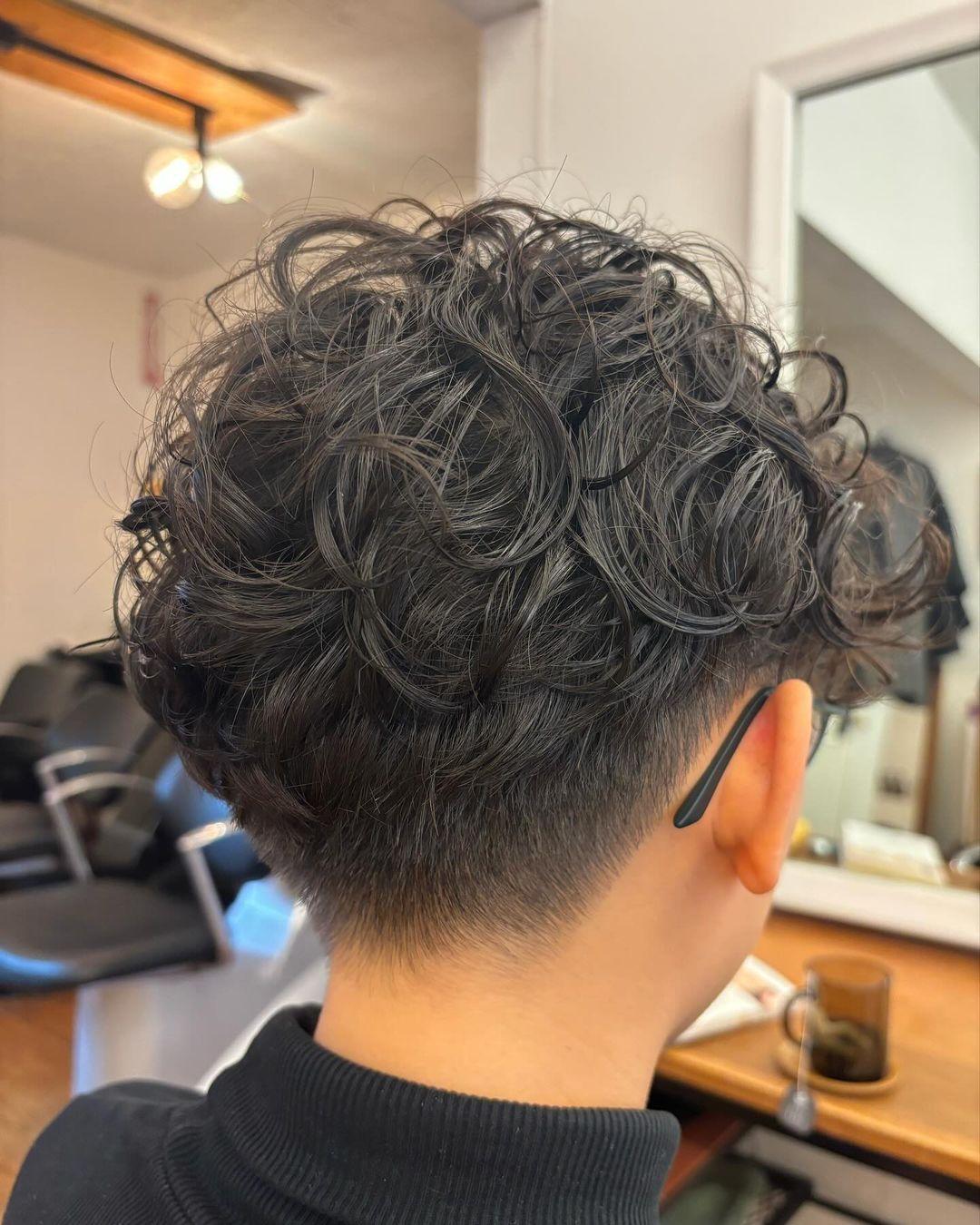 This hairstyle features a cool curly top with natural volume, tapering into a neat undercut at the sides and back. 3