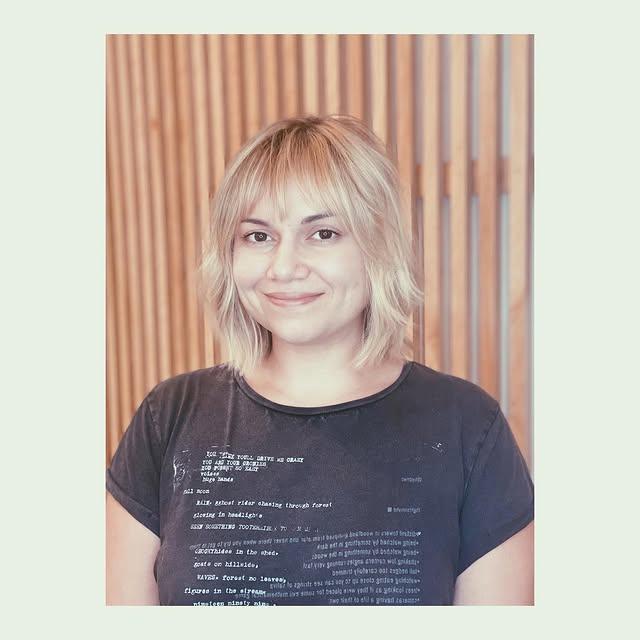 Textured, shoulder-length blonde bob with bangs, creating a modern shaggy look.