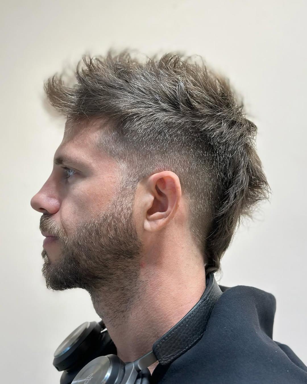 An edgy, textured mohawk with a high fade, featuring dark brown, wavy hair with significant volume on top and subtle tapering at the back. 1