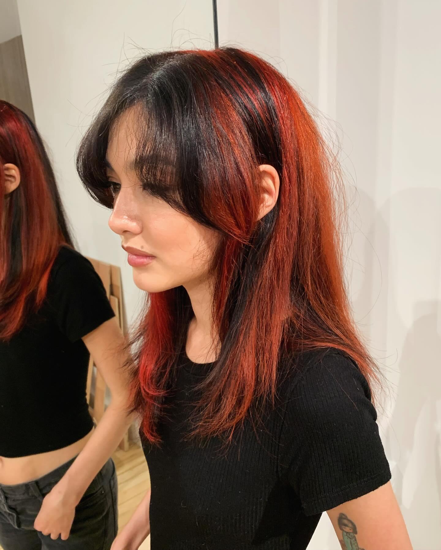A long, straight hairstyle featuring bold black and red hues. It is accented with soft layers and fringe bangs, offering a striking and elegant contrast. 2