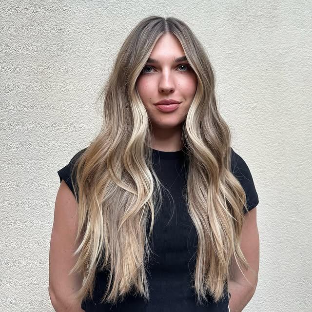 Long, flowing waves with a seamless balayage that blends light brown roots into blonde highlights.