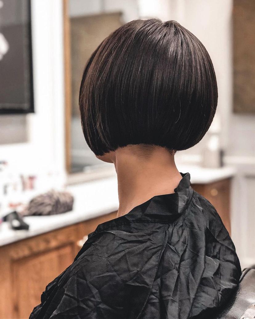 An elegant, short, dark brown bob with a sleek, straight texture, where the blunt cut line sits just above the jawline, with a shaved undercut.
