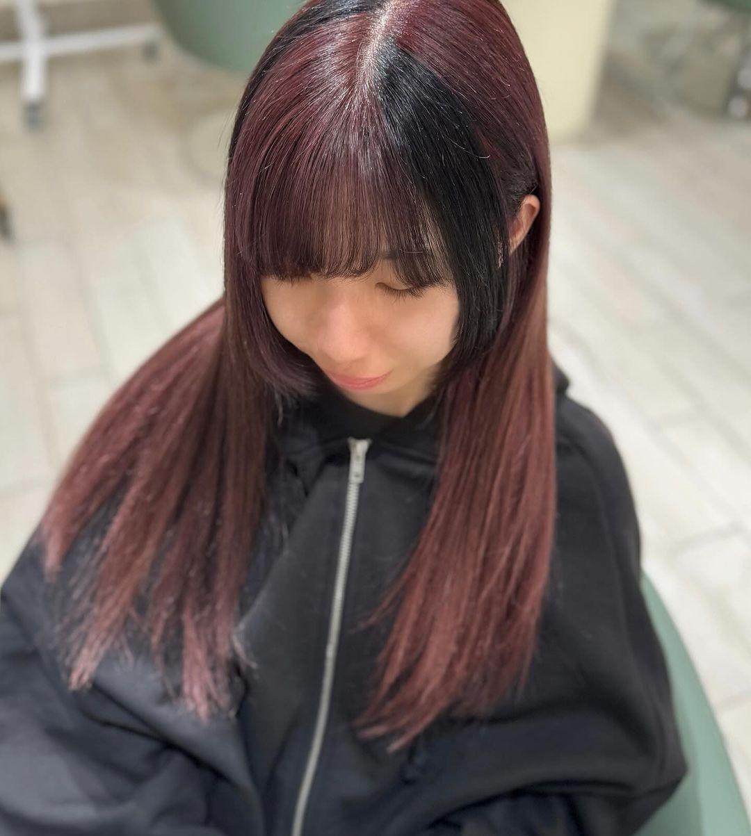 Long, straight burgundy hair with hints of black, featuring a prominent fringe and sophisticated ombre effect. Layers add movement and volume, enhancing the silky texture and polished finish. 4