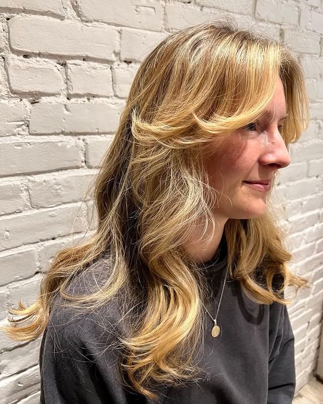 Long, wavy layers that frame the face with trendy curtain bangs and blonde highlights.