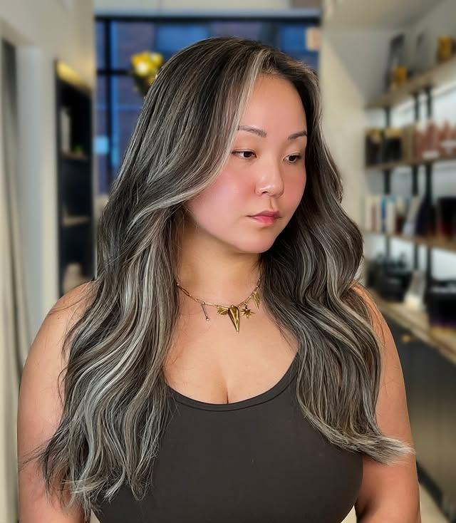 Long wavy hair with face-framing silver streak money piece highlights.