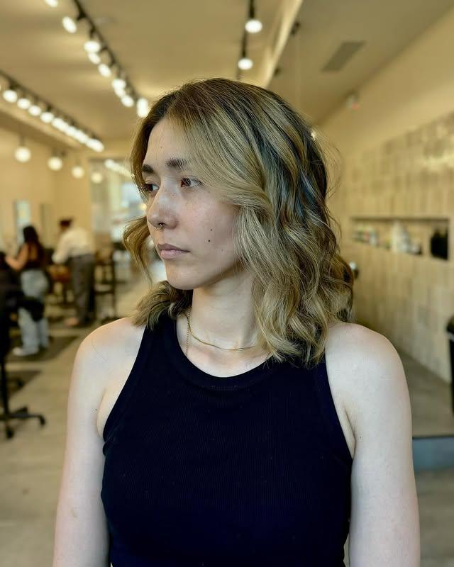 Blonde balayage lob with face-framing curtain bangs by Little Lion Salon