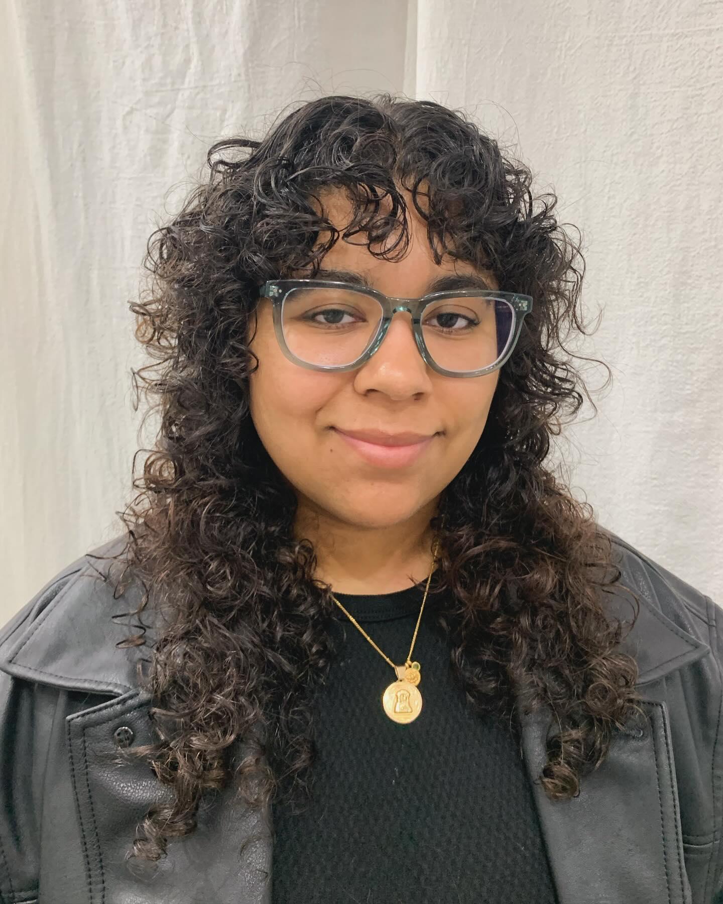 Long, dark brown curly hair with a full fringe and cascading voluminous ringlets. 1