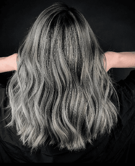 Long wavy hair with an ombre transition from dark black roots to silver and gray tones