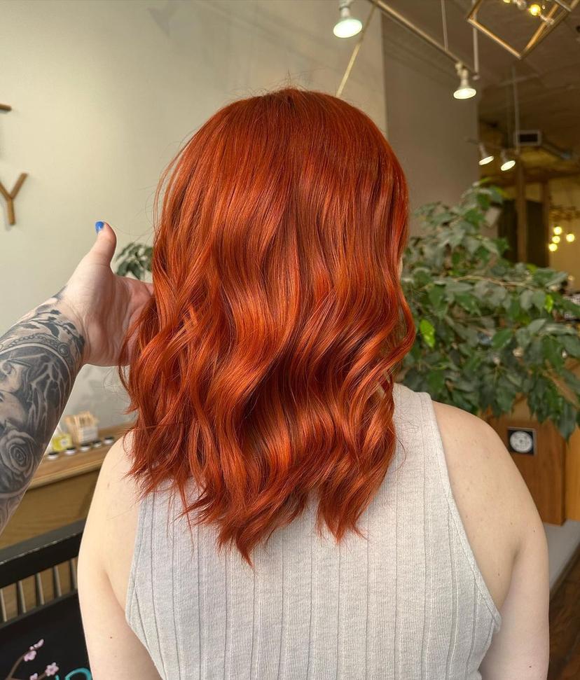 Medium-length wavy hair with vibrant red and fiery orange hues and loose waves.