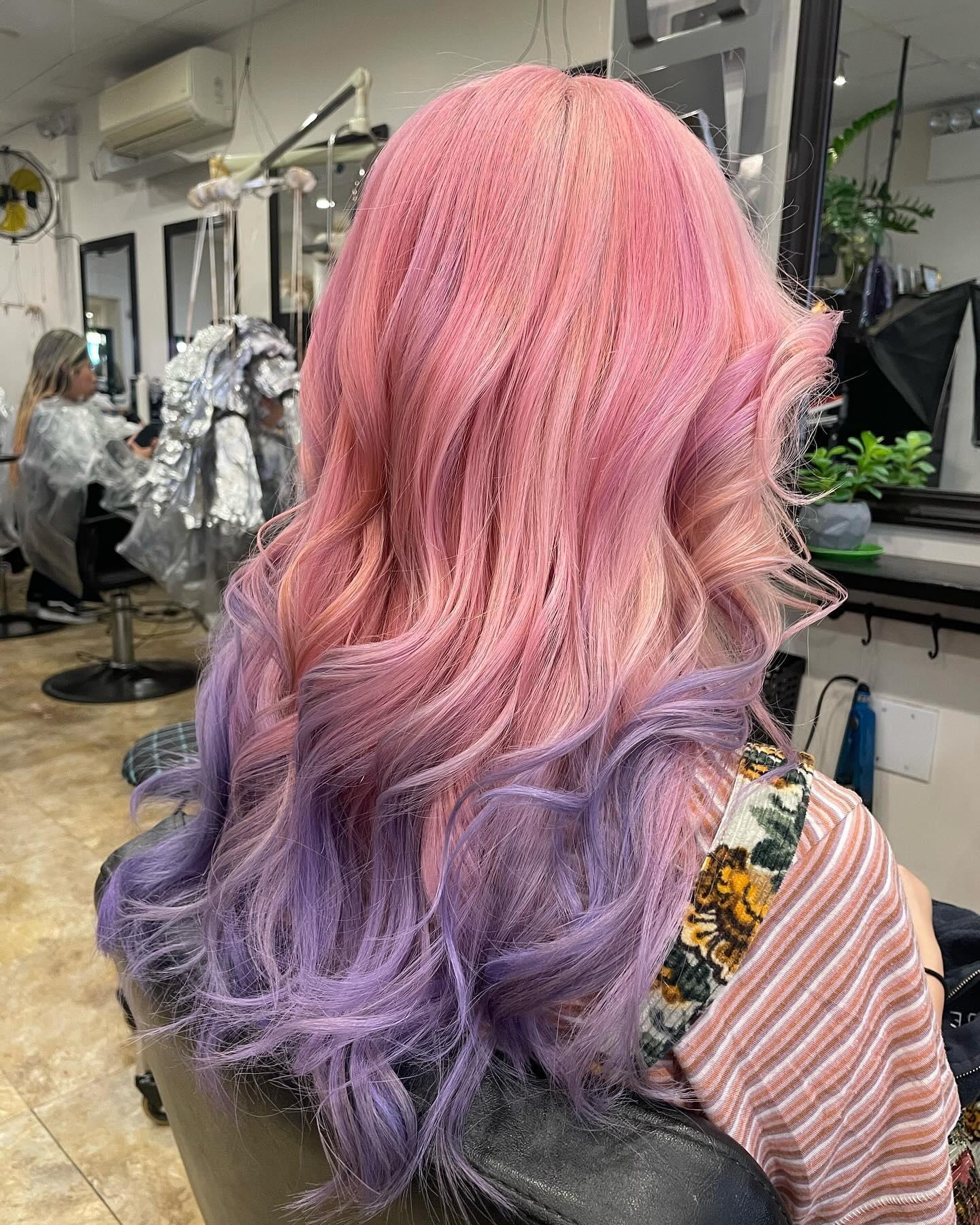 A long, wavy hairstyle featuring an ombre blend of pastel pink, lavender, and purple, characterized by soft waves and vibrant color transitions. 1