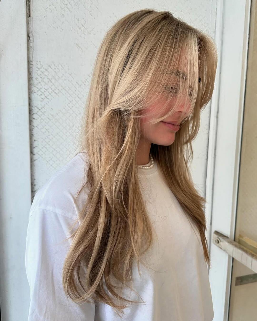 Long, wavy, blonde hair with side-swept bangs and layered waves, featuring natural volume and a beachy texture. 1
