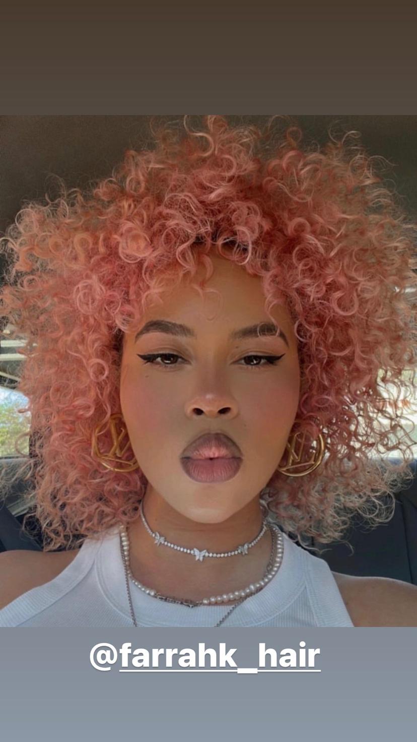 A curly bob haircut with defined curls and pink color.