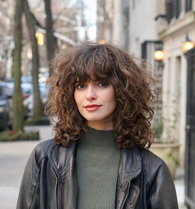 Shaggy layered curly bob with volume and retro-inspired bangs.