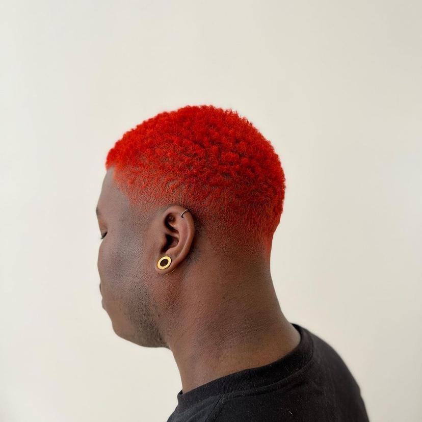 Short, curly hair dyed bright red with a distinct fade on the sides.