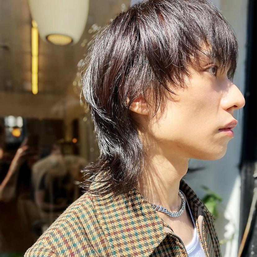 Dark brown, medium-length hair styled in an edgy modern mullet with layered, wavy texture and tapered sides, known as a Wolf Cut.