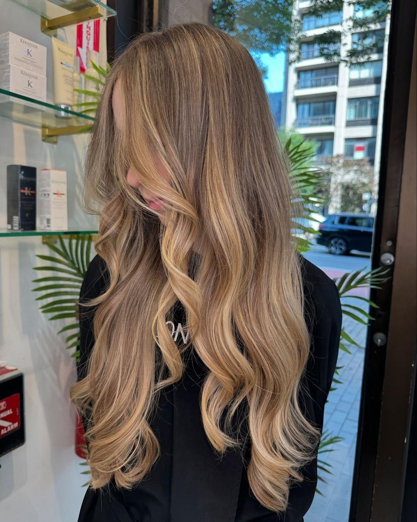 Very long, wavy hair with a blend of dark blonde and golden blonde tones. Soft waves, voluminous, layered, side part.