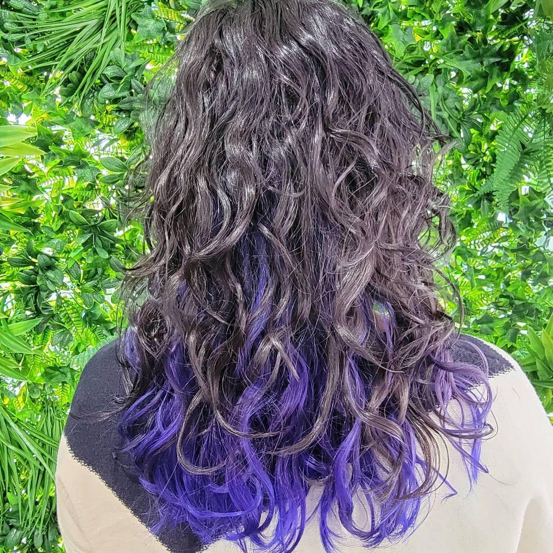 Medium length, curly hair with black base color highlighted by bold purples cascading through the curls and layered tips for added dimension. 3