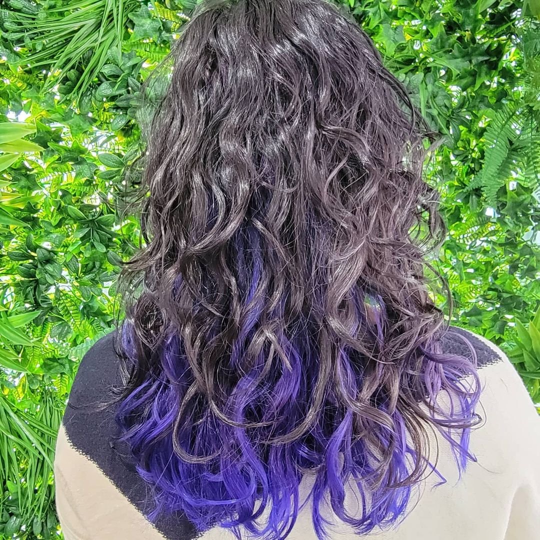 Medium length, curly hair with black base color highlighted by bold purples cascading through the curls and layered tips for added dimension. 3